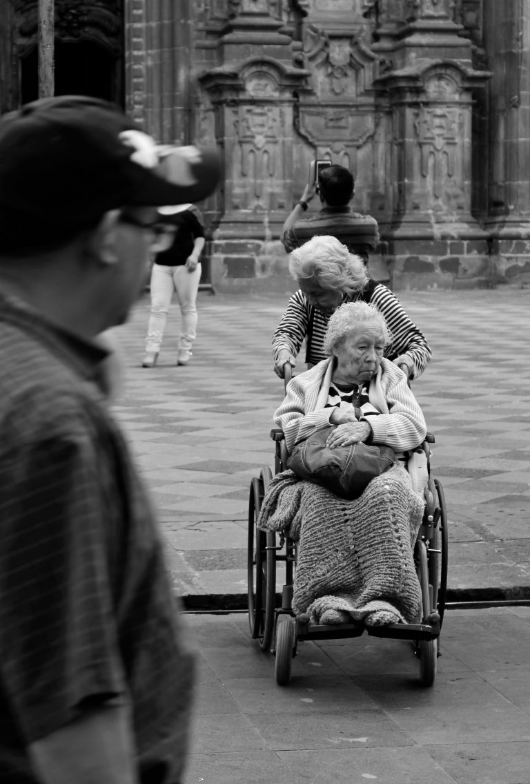 grayscale photography unknown person riding on wheelchair outdoors